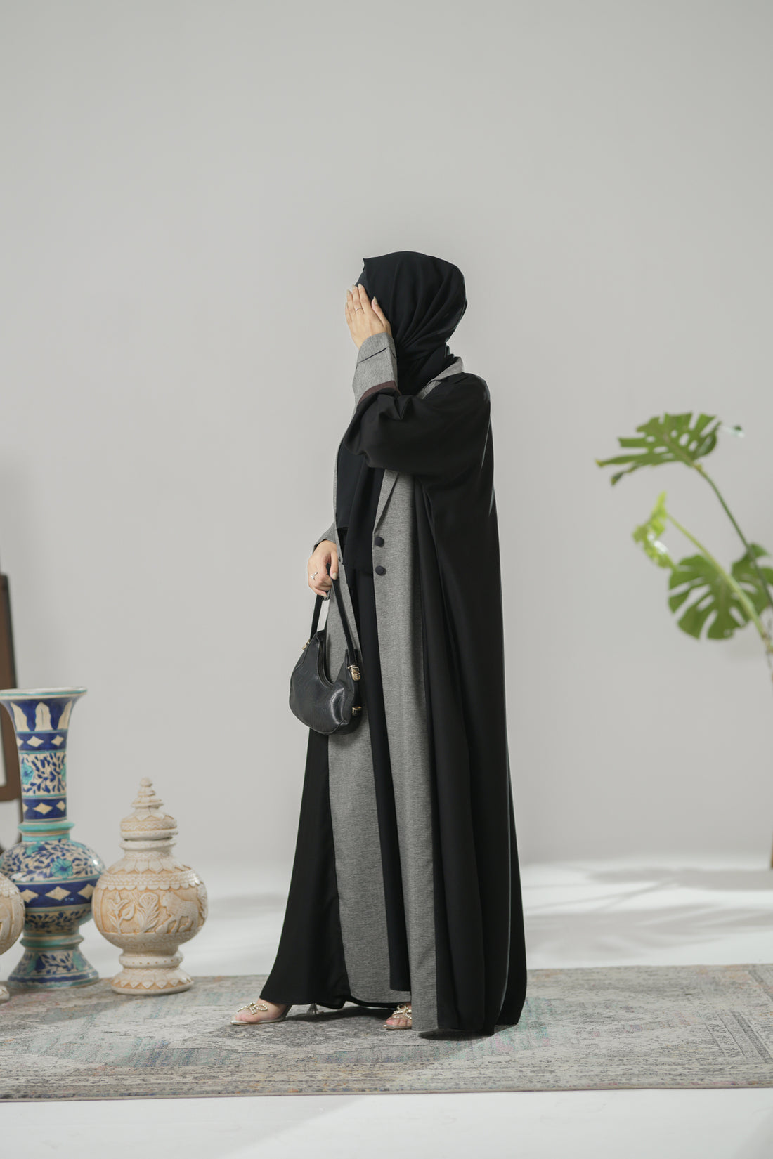 Woman wearing a black and gray abaya in a room with decorative items.
