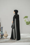 Woman wearing a black and gray abaya in a room with decorative items.