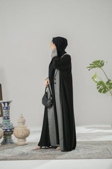 Woman wearing a black and gray abaya in a room with decorative items.