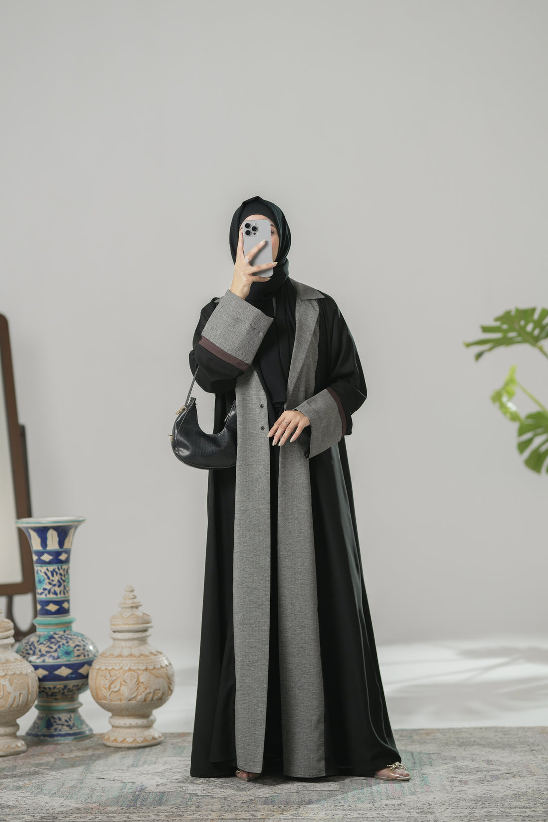 Woman wearing a black and gray abaya in a room with decorative items.