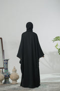 Person wearing a black kaftan abaya standing in a room with decorative items.